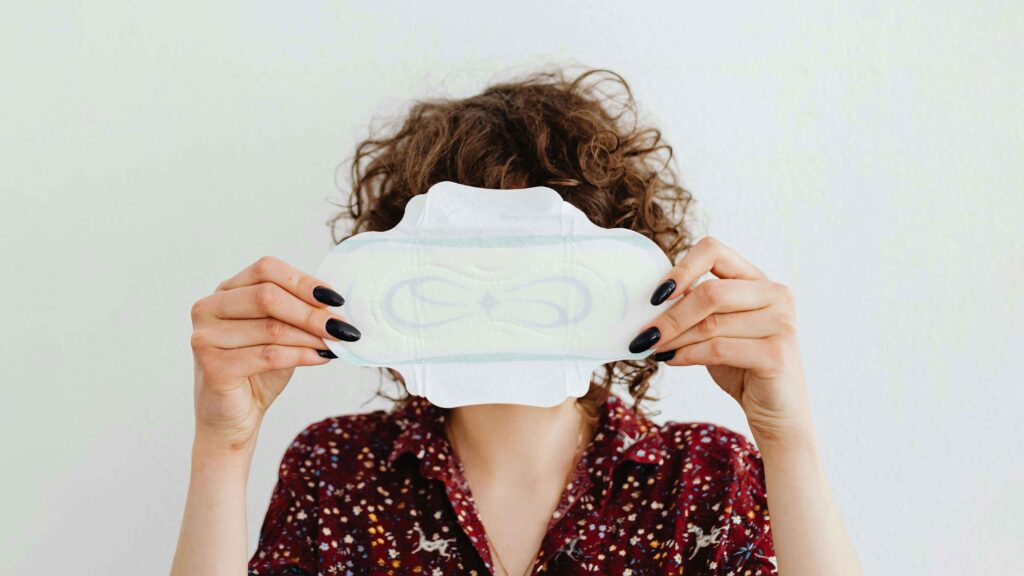 Nő egészségügyi betéttel az arca előtt, vizuális illusztráció a menstruációs szegénység és női egészség témájához.