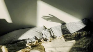 Ágy párnákkal és takaróval, a falra vetülő kézárnyékkal – a nyugtalan alvás és az esti pihenés hangulatának megjelenítése.