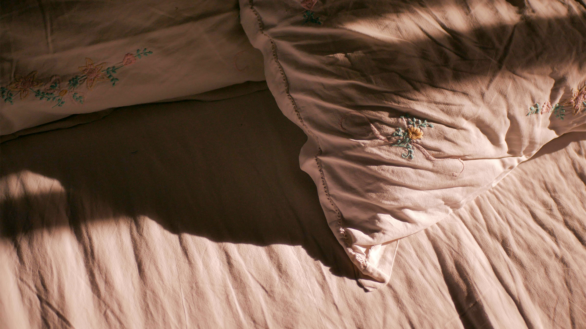 Lágy fényben megvilágított ágy és párnák árnyékokkal, pihenést és nyugodt alvási környezetet idéző hangulatban.